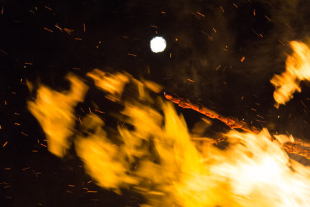 Full moon over a large bonfire with bright orange flames at nightの写真素材