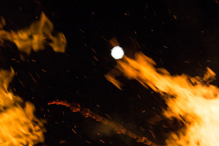 Full moon over a large bonfire with bright orange flames at nightの写真素材