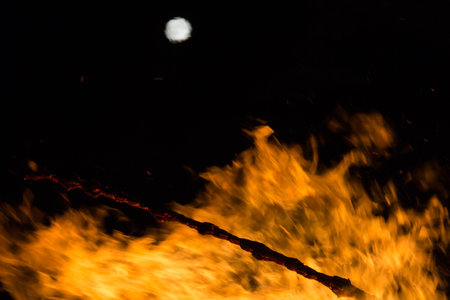 Full moon over a large bonfire with bright orange flames at nightの写真素材