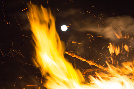 Full moon over a large bonfire with bright orange flames at nightの写真素材