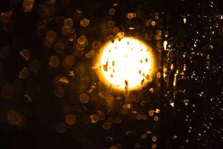 Blurry glowing street light seen through rain-covered glass at night with golden bokeh
