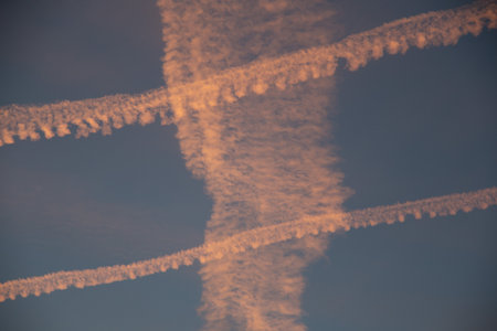 Crisscrossing airplane contrails in the sky during sunset with warm and cool tonesの写真素材