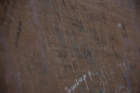 Close-up of weathered brown surface with faint chalk marks and textured scratches in low lig