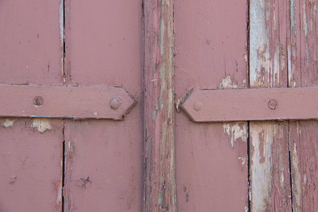 Close-up of weathered pink wooden door with horizontal braces and peeling paint