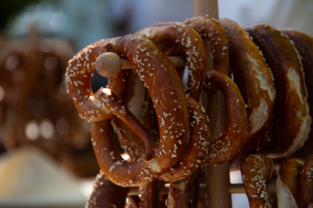 Freshly baked traditional pretzels stacked on a wooden stick with blurred background at an outdoor marketの写真素材
