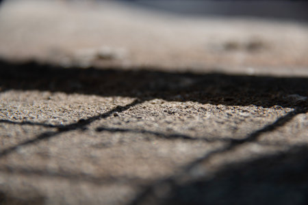 Shadow of a metal fence falling across a sunlit stone ground surface in soft focus