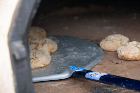 Freshly baked small bread rolls on rustic wooden surface with metal spatula in foregroundの写真素材