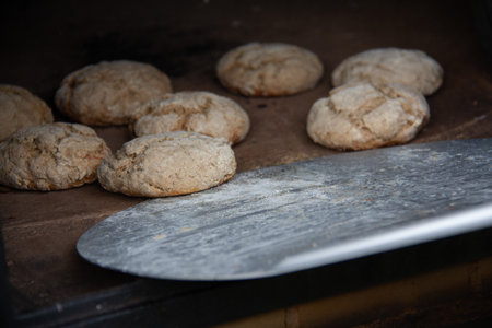 Freshly baked small bread rolls on rustic wooden surface with metal spatula in foreground