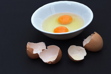 Prepare two chicken eggs in a bowl to cook on black background.