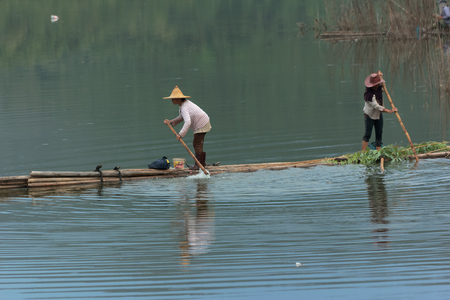 Phayao,Thailand - July 25,2017 : Unidentified two native women are standing on a bamboo raft to help punt on a river at Mae Tam reservoir in Thailand.のeditorial素材