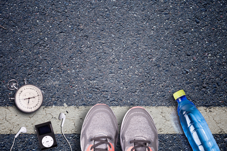Women Running shoes and runner equipment on asphalt. Training on hard surfaces. Runner Equipment stopwatch and music player. The necessary water bottle. Asphalt on the background. Time to running.の写真素材