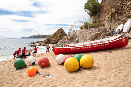 People pull a boat to the shore. Beach and colorful buoys in Lloret de Mar. Boat on the shore and Active holiday time in summer.のeditorial素材