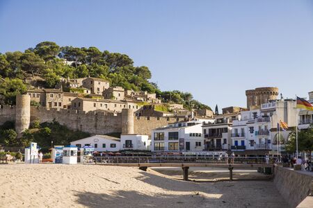 Beach under the castle in Tossa de Mar. People on the seafront near the walls of the old city. The historic city and the castle tower of La Vila Vella. A beautiful Catalan town on the Costa Bravaのeditorial素材