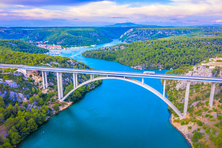 Drone image of the reinforced concrete arch Sibenik Bridge spanning Sibenik Bay near the mouth of the Krka River, with the scenic town of Skradin visible in the distance behindの写真素材