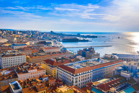 Aerial view of Trieste, Italy, showing the elegant coastline, historic waterfront promenade, and urban layout nestled between the Adriatic Sea and rolling hills of the regionの写真素材