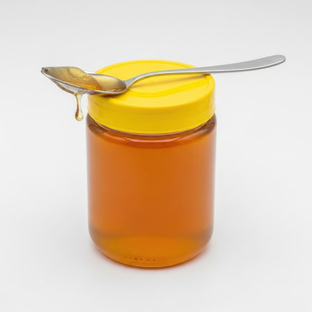 Honey jar with spoon isolated on white backgroundの素材