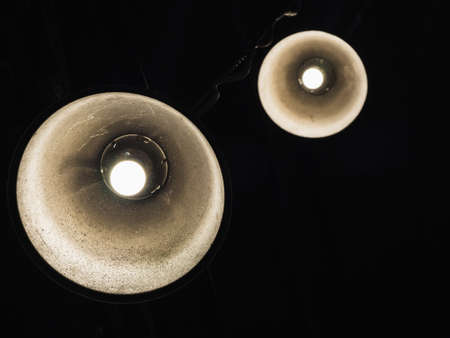 Close up of two conic shape billiard lamps with bulbs hanging in a hipster cafe against black...