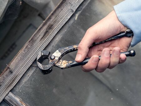 Hands working and holding a pair of pliers and taking out a nail. Repairing old wooden window with a tool. Closeup of home DIYの写真素材