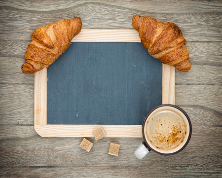 Cup of black coffee with croissant, blackboard on rustic wooden backgroundの写真素材