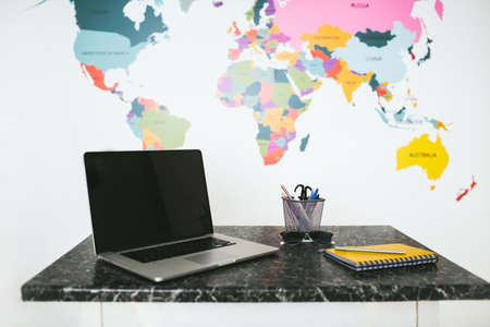 Laptop and notebook on the table in a white background with bright world map.の写真素材