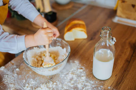 Little girl helping mom bake a cake in the kitchen. Closeup with small cute hands and a bowl. Bottle...