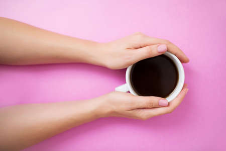 Flatlay with black coffee in a white mug. Woman hands with manicure on a pink background.の写真素材