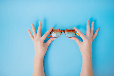 Female hands gently holding glasses on blue background.の写真素材