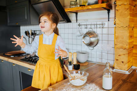 A little smiling girl getting ready to bake a cake in the kitchen. A bowl with flour and milk on the table.の写真素材