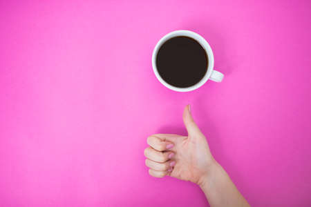 Flatlay with black coffee in a white mug. Woman hand showing thumb up sign on a pink background.の写真素材