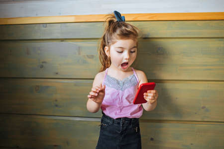 Portrait of an excited little girl holding mobile phone and looking at the screen.