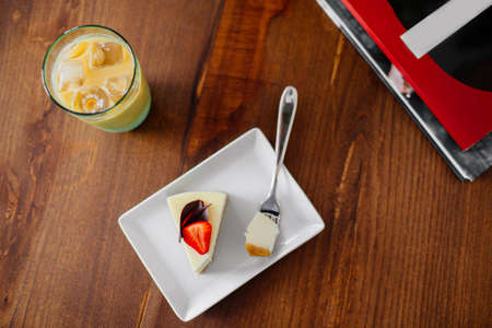 A slice of delicious cheesecake with strawberry on top. Cold frappe with ice beside, top view.の写真素材