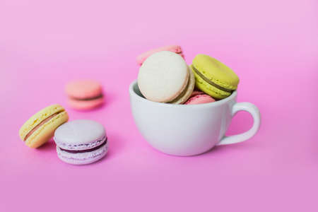 Creative image of sweet colorful French macaroon biscuits in a white mug on pink background.の写真素材