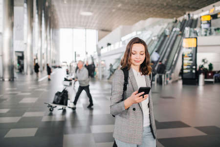 Young girl at the airport walks, looking at her smartphone smiling.の写真素材