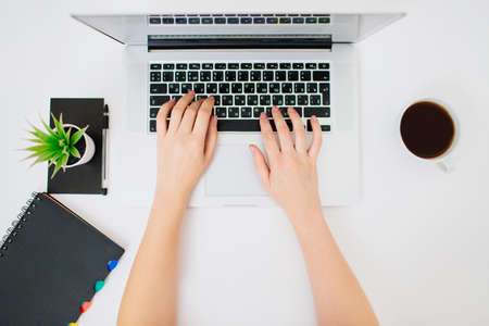 Top view of female hands typing on a laptop keyboard. Coffee, plant and notebook beside.の写真素材