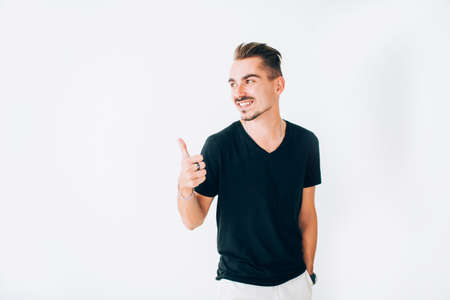 Cheerful smiling young man in a black t-shirt showing away thumb up, isolated on white background.の写真素材