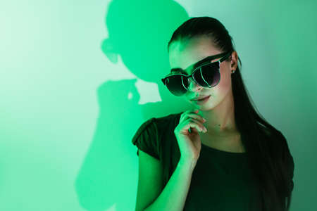 Night portrait of a young beautiful girl with reflection in sunglasses in green neon light.の写真素材