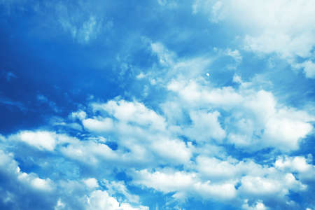 Blue sky with white clouds all over the image with the moon seen.
