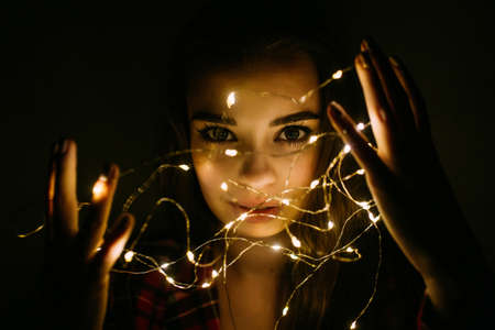 Young woman standing in the dark with fairy garlands lights.の写真素材