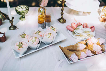 Tasty birthday cupcakes of pink pastel color with stars on top, and other sweet confections, lying on the table. Festive composition.の写真素材