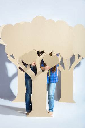 Boy with girl hiding behind cardboard tree and holding a cardboard heart. Love concept.の写真素材