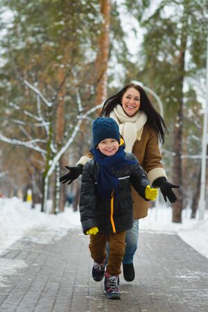 Happy family in winter clothing. Smiling son runs away from his mother outdoor.の写真素材
