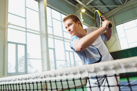 Low angle view of determined young man playing tennis indoor.の写真素材