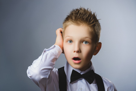 Close up Thoughtful Young Boy Looking Up with Hand on the Face Against Gray Background with Copy Space.の写真素材