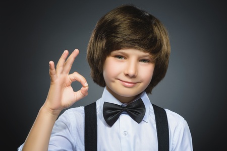 Happy boy. Closeup Portrait of handsome teenager smiling and show Ok over grey background.の写真素材