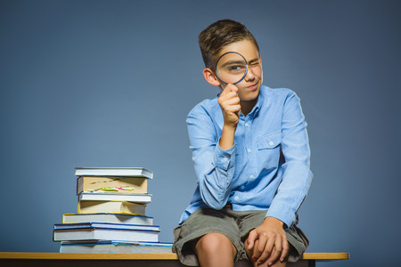 school concept. doubt boy sitting on desk and looking into a magnifying glass.の写真素材