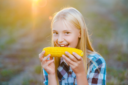 Happy girl eating healthy corn on the cob.の写真素材