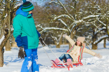 Happy boy and girl sledding in winter outdoorの写真素材
