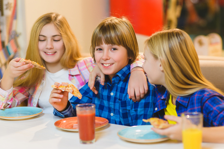 smiling boy and girls eating pizza or drinking juice indoorの写真素材