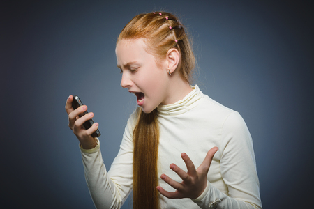 Angry redhead girl with cell phone. isolated on grayの写真素材