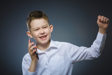 Closeup Portrait of happy boy with mobile or cell phone on gray backgroundの写真素材